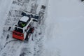 Skid steer loader removes snow from the city streets. Top view of the road with cars and snow blower. Seasonal work in winter Royalty Free Stock Photo