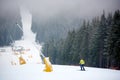 Skier doing freeriding descenting in snowfall on mountain slope with chairlift among dense coniferous forest. Back view