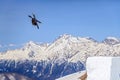 Skier flying from a ski jump making figure on blue sky and snowy mountain peaks background Royalty Free Stock Photo