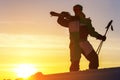 A skier holds skis in his hands against the sunset sky