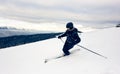 Skier inclining turning on snow-capped mountain peak. Extreme skiing concept. Mountains view. Grey sky on background.