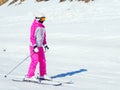 A skier in a pink suit and with a closed face rides a straight track on a sunny winter day