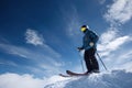 Skier standing on mountain peak ready to descend under bright blue sky with fluffy clouds in winter Royalty Free Stock Photo