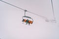 Skiers on a chairlift ascend a mountain through thick fog