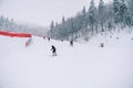 Skiers descend the mountainside along the red fence on the Kolasin 1600 slope. Montenegro Royalty Free Stock Photo
