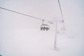 Skiers on a four-seater chairlift ride up the mountain through the fog Royalty Free Stock Photo