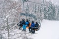 Skiers in helmets and ski suits ride up the slope above the snowy forest