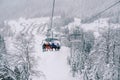 Skiers ride uphill on a four-seater chairlift above snow-covered trees Royalty Free Stock Photo
