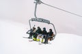 Skiers with ski poles in their hands ride a four-seater chairlift up a snowy mountain slope Royalty Free Stock Photo