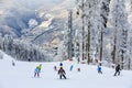 Skiers and snowboarders ride on ski slope in Sochi mountain ski resort on snowy winter mountain scenic background. Caucasus