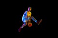 Skilled, athlete man, basketball player mid-air dribbling in motion against black studio background in mixed neon light. Royalty Free Stock Photo