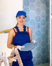 Skilled builder female in work clothes posing with ceramic tiles and construction tools while repair and decoration in