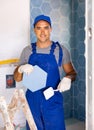 Skilled builder in work clothes posing with ceramic tiles and construction tools while repair and decoration in