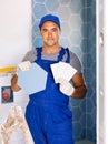 Skilled builder in work clothes posing with ceramic tiles and construction tools while repair and decoration in