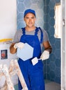 Skilled builder in work clothes posing with ceramic tiles and construction tools while repair and decoration in