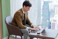 Skilled businessman working with laptop near window with skyscraper. Ornamented. Royalty Free Stock Photo