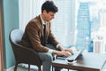 Skilled businessman working with laptop near window with skyscraper. Ornamented. Royalty Free Stock Photo