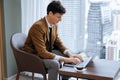 Skilled businessman working with laptop near window with skyscraper. Ornamented. Royalty Free Stock Photo