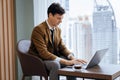 Skilled businessman working with laptop near window with skyscraper. Ornamented. Royalty Free Stock Photo