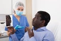 Woman beautician in mask examining face skin of afro american male patient Royalty Free Stock Photo