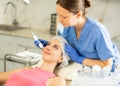 Skilled female dermatologist performing cosmetology procedure for young woman, RF lifting and microcurrents for facial