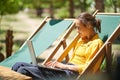 Skilled freelance woman using laptop computer while sitting on sun lounger outdoors, online working digital