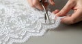 Skilled hands carefully trim the delicate edge of white floral lace fabric with small scissors Royalty Free Stock Photo