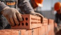 Construction workers wearing protective gloves and helmets carefully placing red bricks while building a sturdy brick wall under Royalty Free Stock Photo