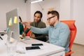 Skilled male leader in eyeglasses helping new African female worker with computer corporate software application in Royalty Free Stock Photo