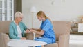 Skilled nurse in blue uniform puts digital blood pressure monitor on senior woman hand in light office Royalty Free Stock Photo