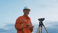 Skilled surveyor in orange jumpsuit works with dumpy level