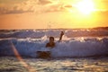 Carefree boy surfing at wave at colourful sunset
