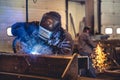 Skilled welder is seen at work in a large industrial factory, using a welding machine with sparks