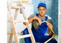 Skilled workman wearing in blue construction overalls sitting squat and repairing shower head in bathroom Royalty Free Stock Photo