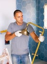 Skilled workman wearing ordinary clothes repairing shower head in bathroom