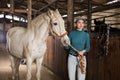 Young female farmer holding reins leading horse through stable Royalty Free Stock Photo