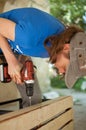 Skilled young female worker is using power screwdriver drilling during construction wooden bench gender equality Royalty Free Stock Photo