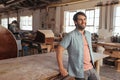 Smiling young woodworker leaning on a table in his workshop