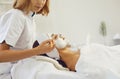 Skillful female beautician applies a mask on a woman`s face with a cosmetic brush.