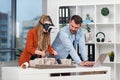 Skillful male architect working on laptop while his female colleague in VR glasses analysing mock-up of future building. Royalty Free Stock Photo