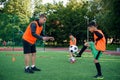 Skillful teen player in football uniform working out the kicking ball together with his experienced coach on sport field