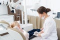 A skillful pediatric dental specialist is examining the teeth of a child. The woman is sitting near the girl trying to