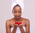 Skin as soft as rose petals. A studio shot of a beautiful young woman holding red petals and wearing a towel on her head Royalty Free Stock Photo