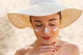 Skin care. Beauty Concept. Young pretty woman applying sun cream and touch own face. Female in hat smear sunscreen lotion on skin. Royalty Free Stock Photo