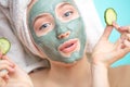 Skin care. Cheerful female with clay mask on face and cucumber slices