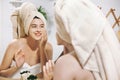 Skin Care concept. Young happy woman in towel making facial massage with organic face scrub and looking at mirror in stylish