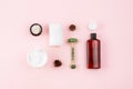 Skin care products on pastel pink surface. Shampoo or cosmetic lotion bottle, jade roller, towel, open cream jar