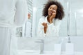 Skin care. Woman applying face cream looking in bathroom mirror