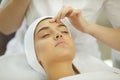 Hands of cosmetologist checking skin elasticity or making facial cleaning for young relaxing woman