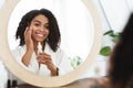 Skin Hydration. Positive black woman applying moisturizing serum on face